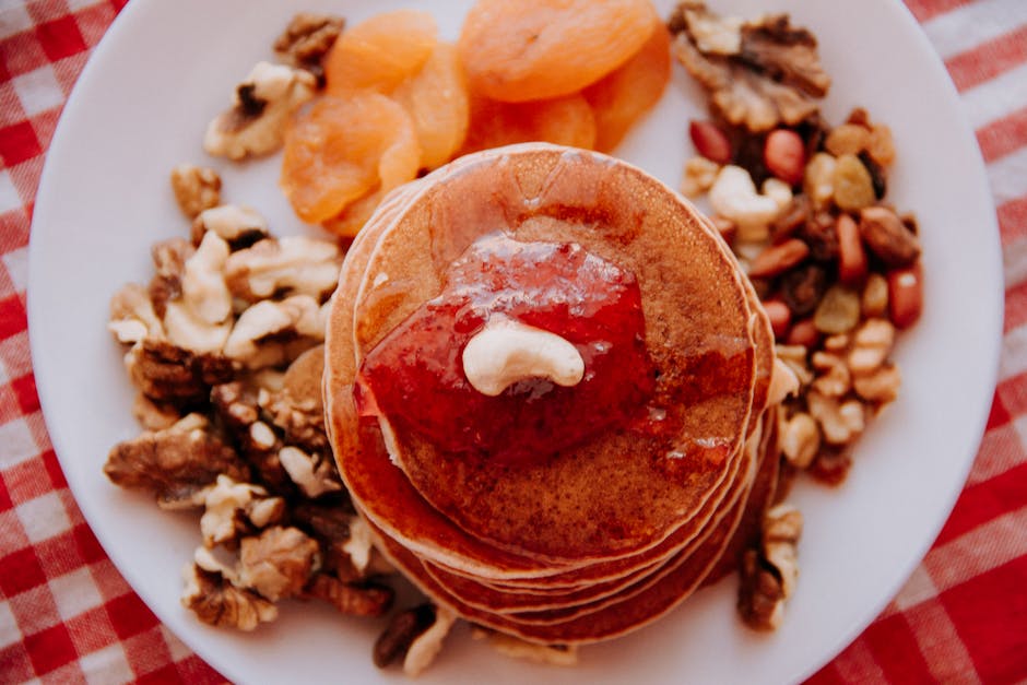 Delicious pancakes topped with jam, cashew, walnuts, and dried fruit on a checkered cloth.